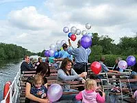 A group of children and young people with balloons, enjoying a boat trip on the River Thames