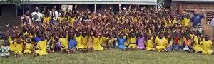 A large group of children and Rotary members outside Rwabagabo school waving their hands