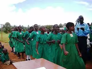 A group of schoolchildren, all dressed in green uniforms, taking part in a welcoming celebration at Mugungulu school