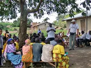 A group of men and women sit in the shade of a tree listening to Rotarian Andrew Bartholomew