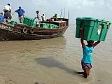 A man wades through water carrying a ShelterBox on his head